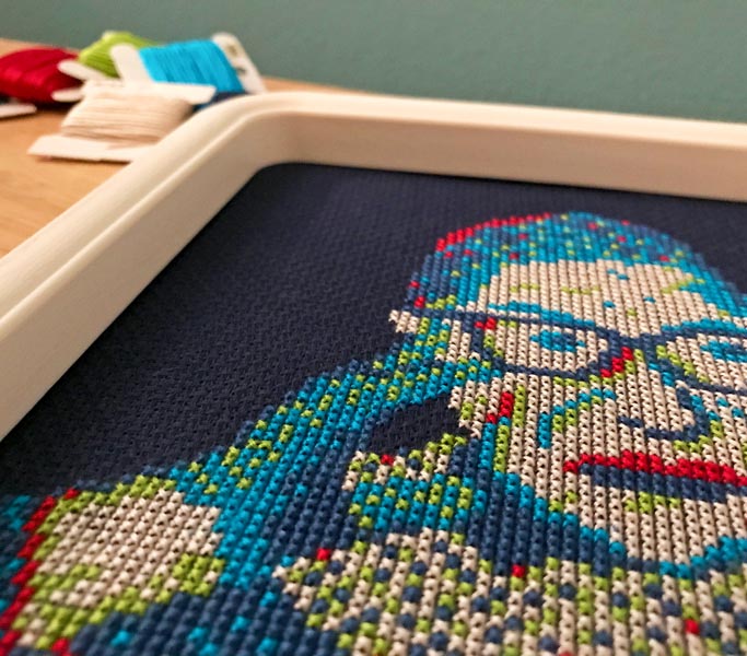 Cross stitch design of Ruth Bader Ginsburg (RBG) in thread colors red, green, and blue (RGB) on navy blue fabric