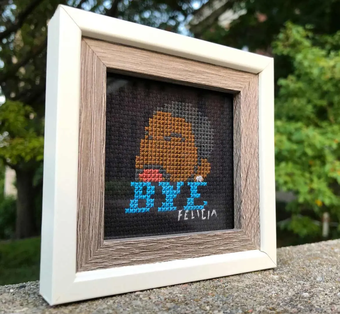 Framed cross stitch design of Ice Cube in “Friday” above words “Bye, Felicia” on black Aida fabric